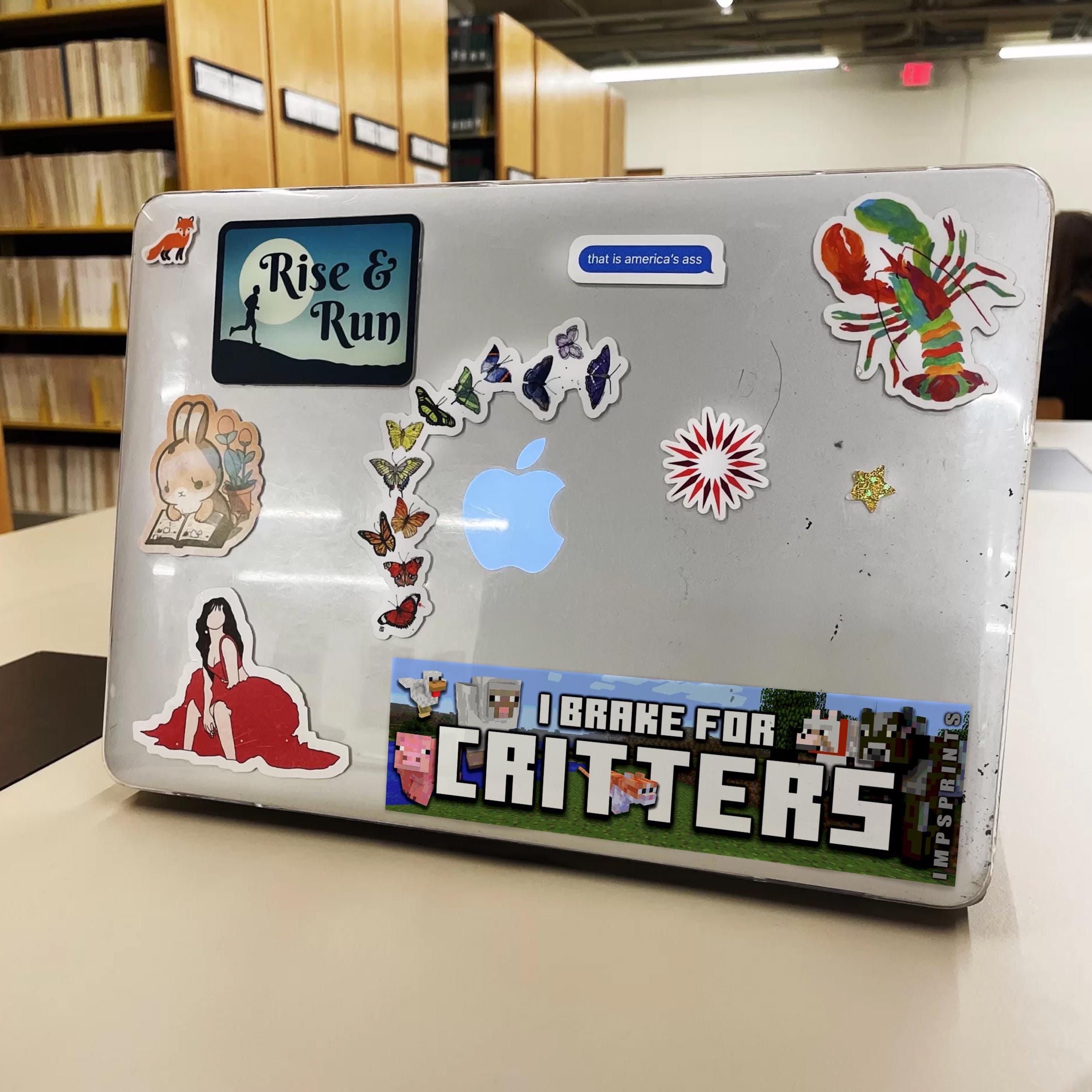 Laptop with various stickers on a table in a library setting