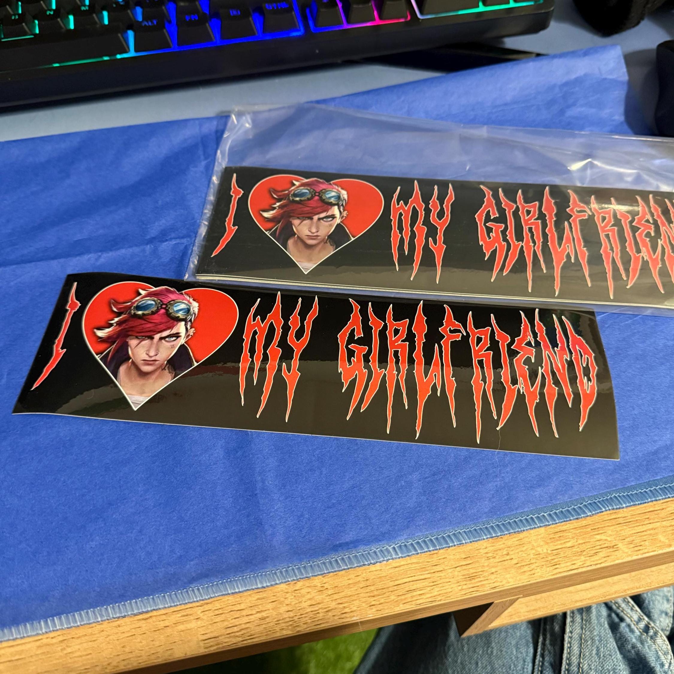 Two bumper stickers with a graphic of vi arcane with red hair and text on a blue surface.