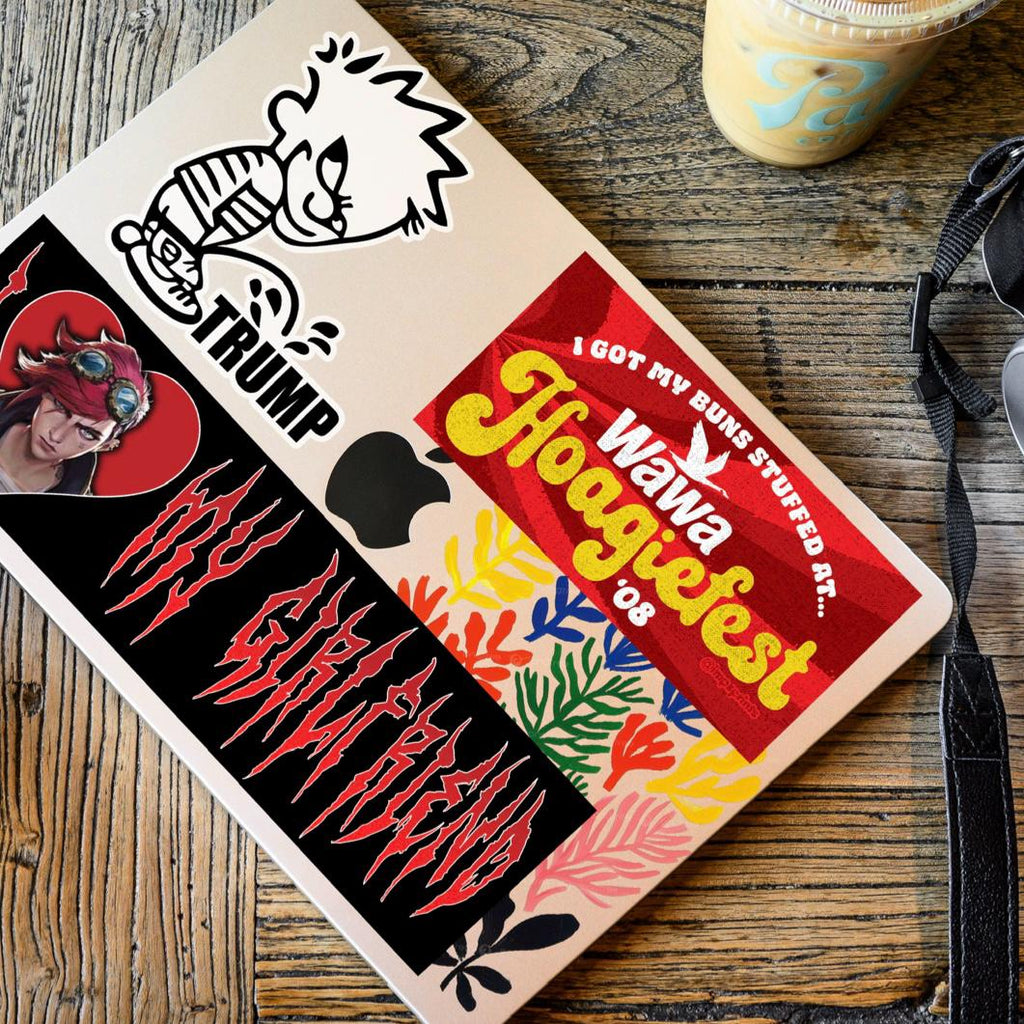 Sticker-covered laptop on a wooden surface with a coffee cup and strap in the background.