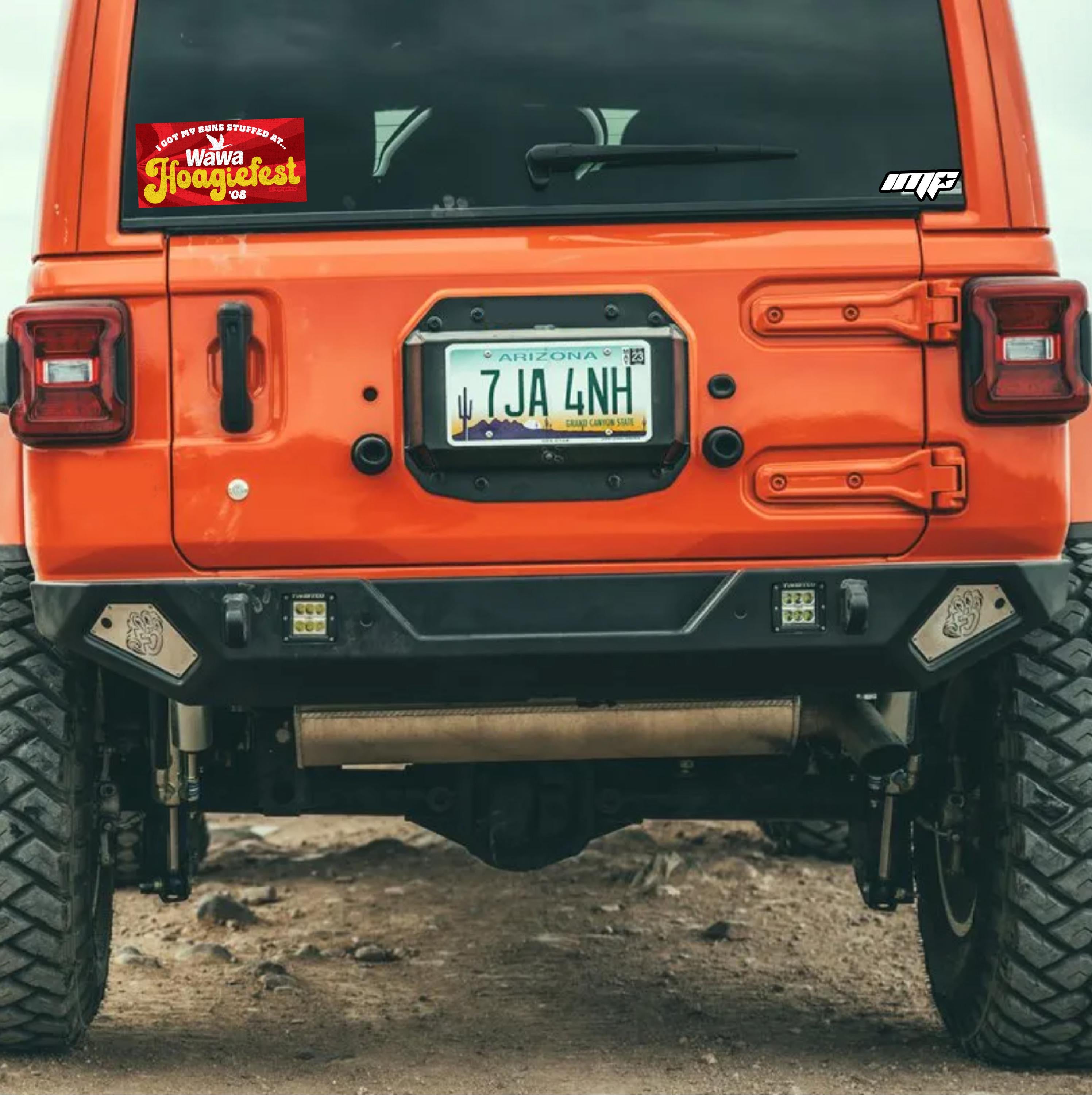 Orange off-road vehicle with visible license plate and wawa woagiefest sticker on a dirt road.
